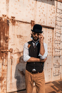 Man holding smart phone while standing against wall