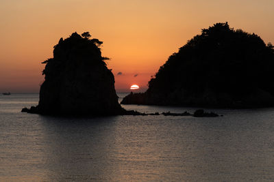 Rock formation in sea against sky during sunset