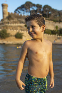 Shirtless boy standing by water outdoors