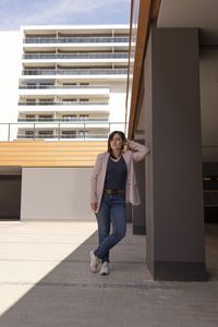 Full length portrait of young woman standing against building