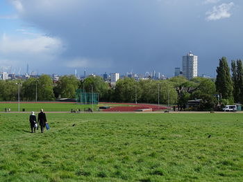 Rear view of men walking on field against sky in city