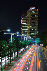Light trails on road against illuminated buildings in city at night
