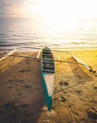 Boat moored on beach against sky during sunset