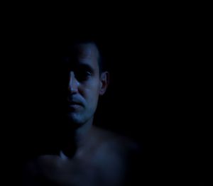 Close-up of shirtless young man against black background