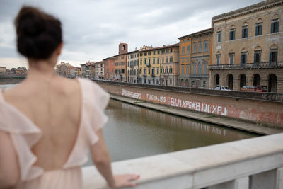 Rear view of woman standing by railing against city