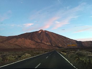 Empty road by mountains against sky