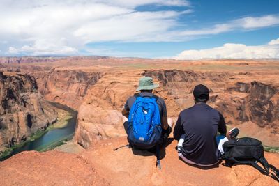 Rear view of friends sitting at horseshoe bend against sky