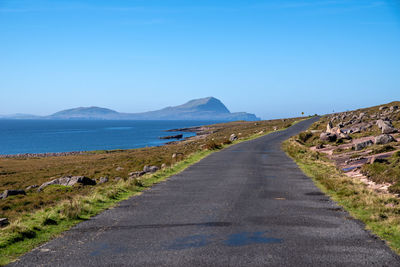 Road by sea against clear blue sky