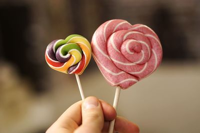 Cropped hand holding heart shape lollipops