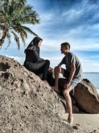 Men sitting on rock by sea against sky