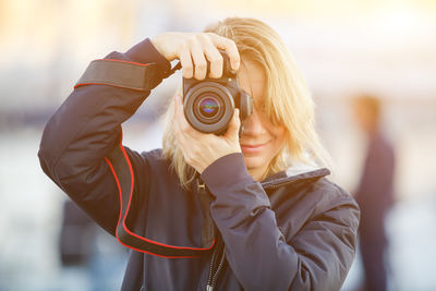 Portrait of smiling woman photographing with digital camera on footpath