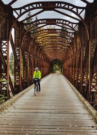 A man in a fluorescent yellow jacket riding a bicycle on a bridge.