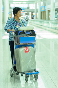Senior woman with luggage in cart standing at airport