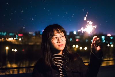 Portrait of young woman standing in city against sky at night