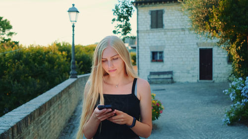 Young woman using phone while standing on plants