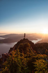 Man standing on rock against sky during sunset