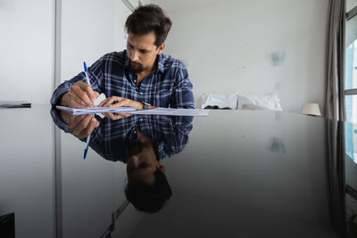 Young man working at home signing papers smiling 