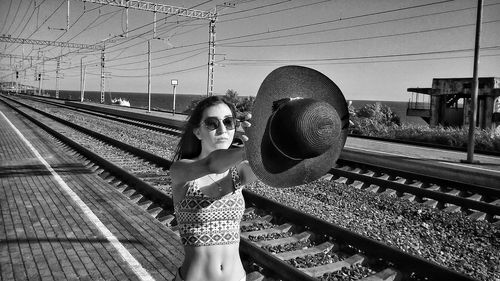 Beautiful woman holding hat while standing on railroad station platform