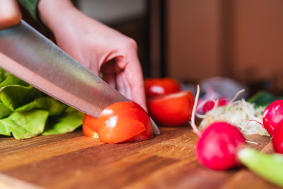 Cropped hand of woman holding tomato on table