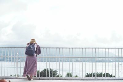 Rear view of woman standing by railing against sky