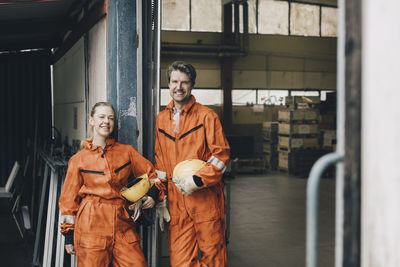 Portrait of confident male and female workers in uniform standing in warehouse doorway