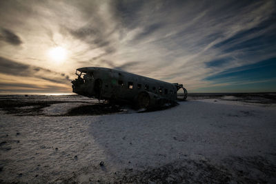 Abandoned car on beach against sky during sunset