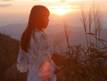 Woman standing on field against sky during sunset