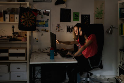 Teenage girl showing something to friend on computer at home