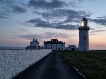 Lighthouse amidst buildings against sky during sunset