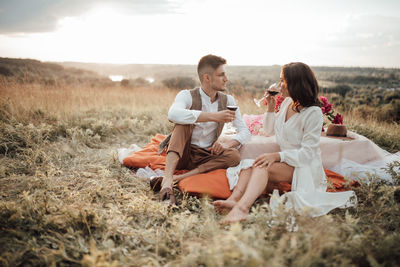 Young couple sitting on land against sky