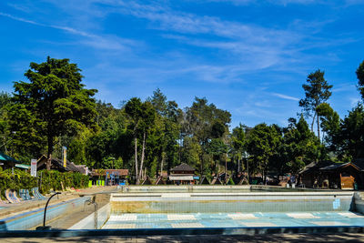 Swimming pool by trees against blue sky