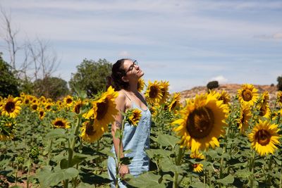 Woman standing on sunflower field against sky