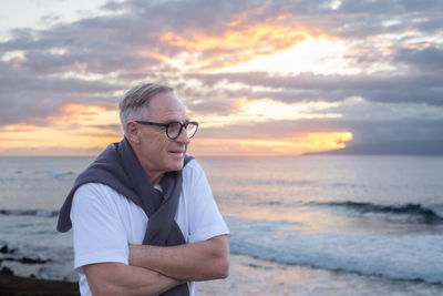 Young man standing at beach against sky during sunset