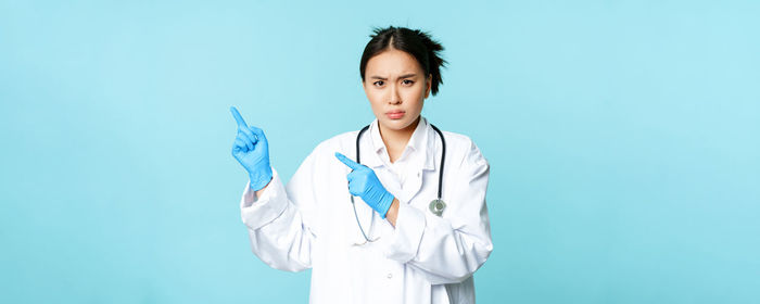 Portrait of young woman standing against blue background