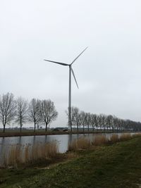 Windmill and bare trees by river against sky