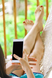 Low section of woman using mobile phone while resting on hammock