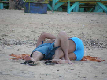 Low section of man relaxing on sand at beach