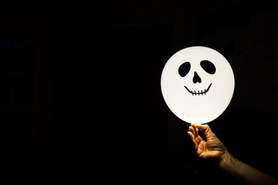 Cropped hand holding balloon with anthropomorphic face over black background