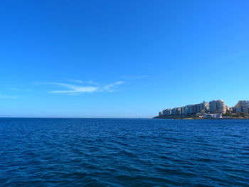 Scenic view of sea by buildings against blue sky