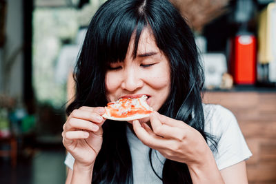 Asian woman eating homemade pizza at restaurant.