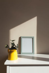 A yellow ceramic jug or vase with eucalyptus branches, empty white photo frames on the table