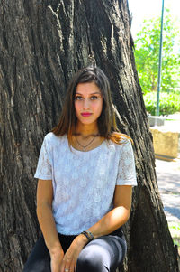 Portrait of beautiful young woman against tree trunk