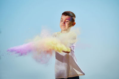 Boy playing with powder paint against sky