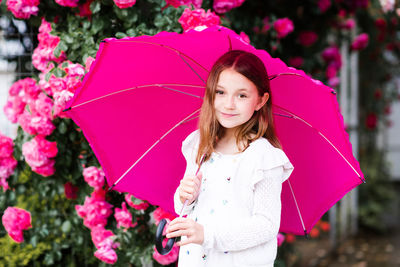 Smiling child girl 8-9 year old hold umbrella standing at city park over rose flowers outdoor
