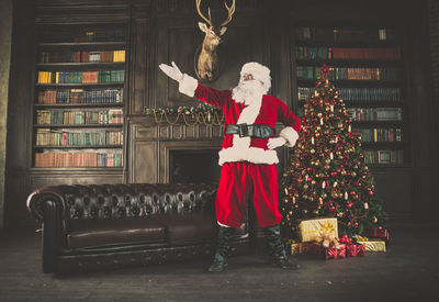 Man wearing santa claus costume standing by christmas tree at home