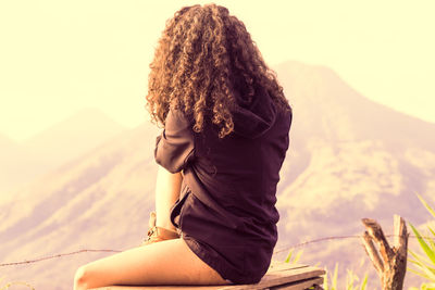 Midsection of woman sitting against mountain against sky