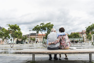 Germany, mannheim, back view of senior couple sitting on a bench hugging each other