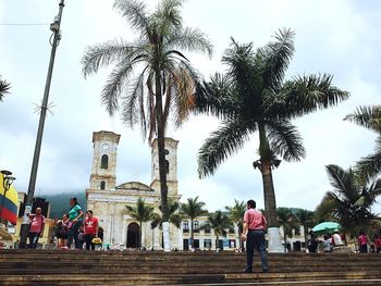 People by palm trees against sky