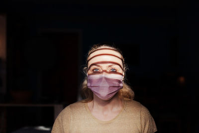 Portrait of young woman wearing mask in darkroom