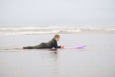 Boy lying on a surfboard on the sand at the beach